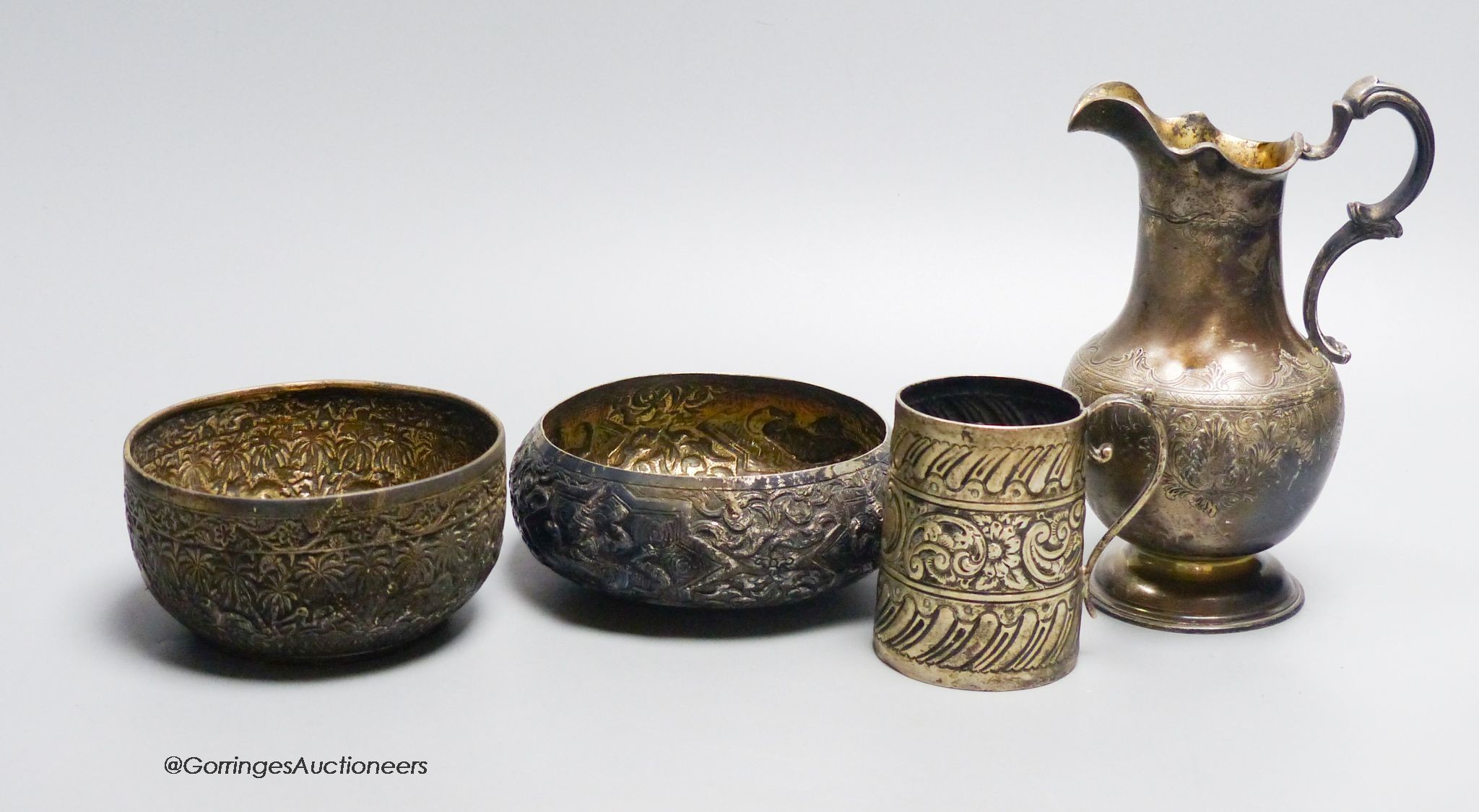 A Victorian engraved silver milk jug, makers mark WM, London 1851, 16 cm, 9.5oz, two Indian white metal bowls and an embossed silver christening mug, marks indistinct, 2.5oz. (4)